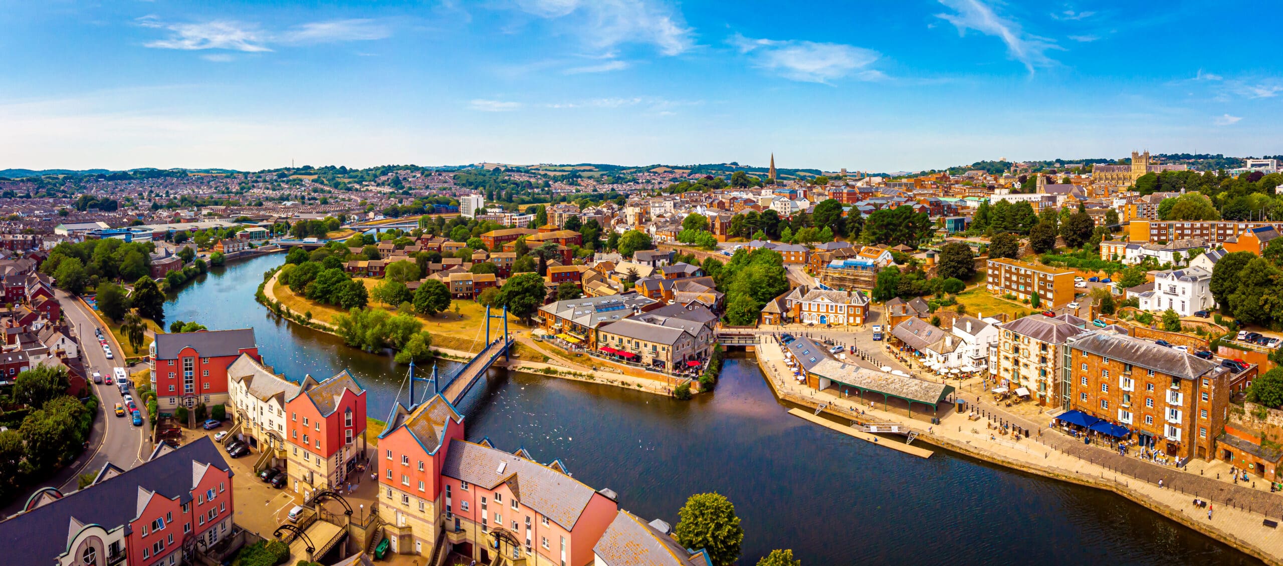 Aerial view of a vibrant city with colorful buildings, winding river, lush greenery, and people walking on a sunny day—where inspiration for bespoke bathrooms or your next bathroom renovation comes naturally.