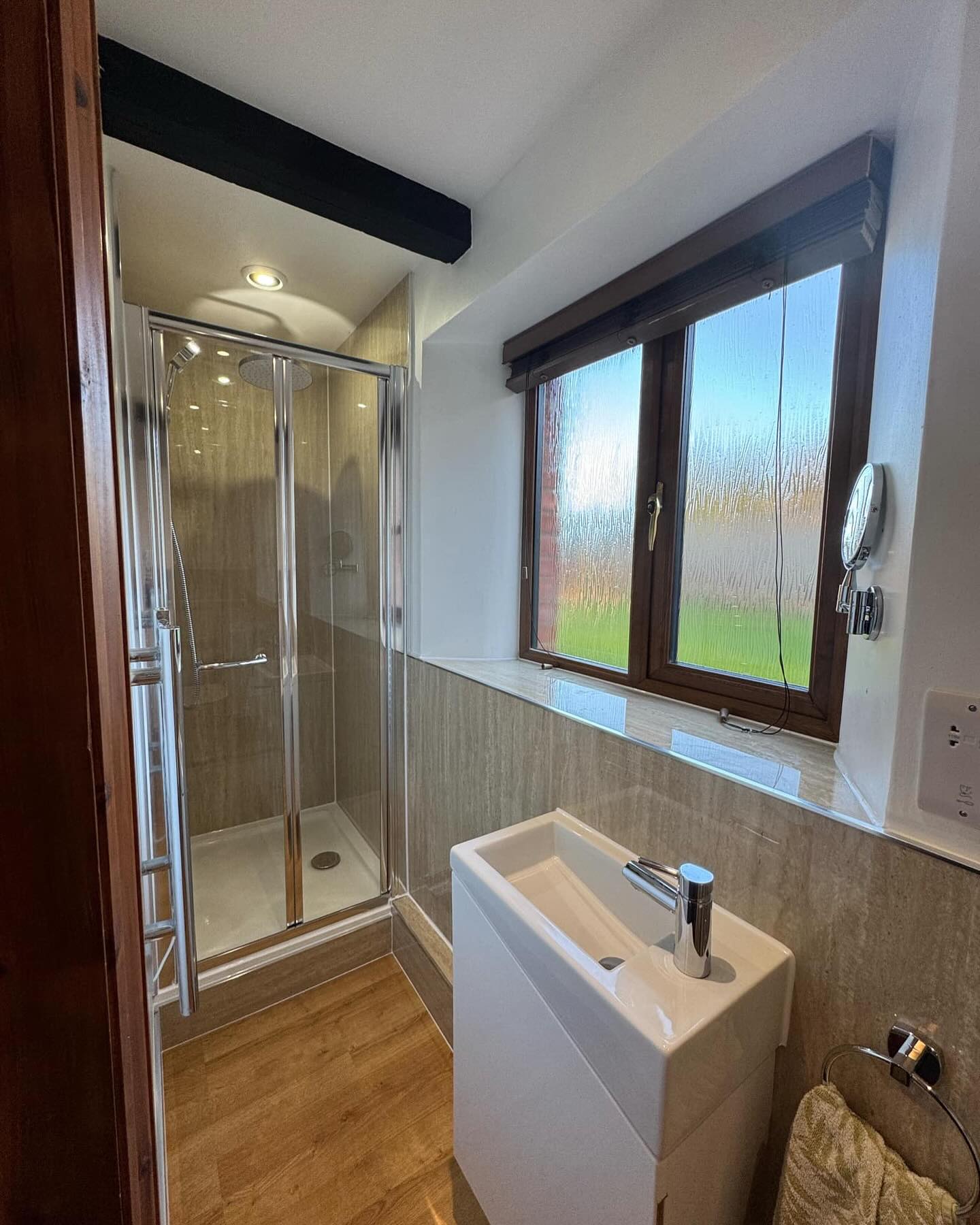 Modern bathroom with a glass shower enclosure, beige tile walls, wood-like flooring, and a white rectangular sink—experience bespoke bathrooms designed with style, just like those displayed in a top bathroom showroom.