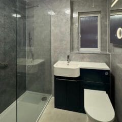A modern bathroom with grey walls, a glass shower enclosure, and a white sink set on a dark vanity—perfect inspiration for your next bathroom renovation or visit to a bathroom showroom. The minimalist design features sleek lighting and fixtures throughout.