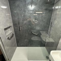 Modern walk-in shower with gray marble walls, a glass partition, rainfall and handheld showerheads, built-in shelf, grab bars, and a white shower base perfect for BESPOKE BATHROOMS in any contemporary bathroom installation.