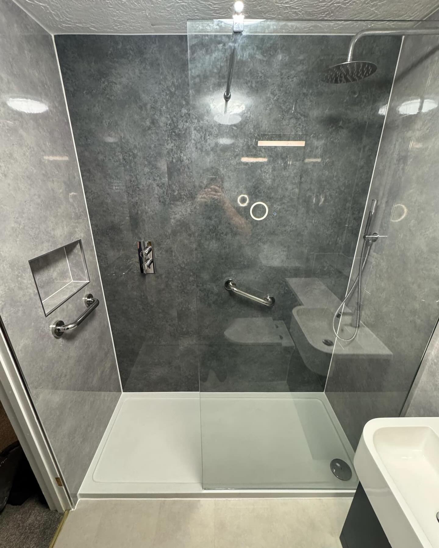 Modern walk-in shower with gray marble walls, a glass partition, rainfall and handheld showerheads, built-in shelf, grab bars, and a white shower base perfect for BESPOKE BATHROOMS in any contemporary bathroom installation.